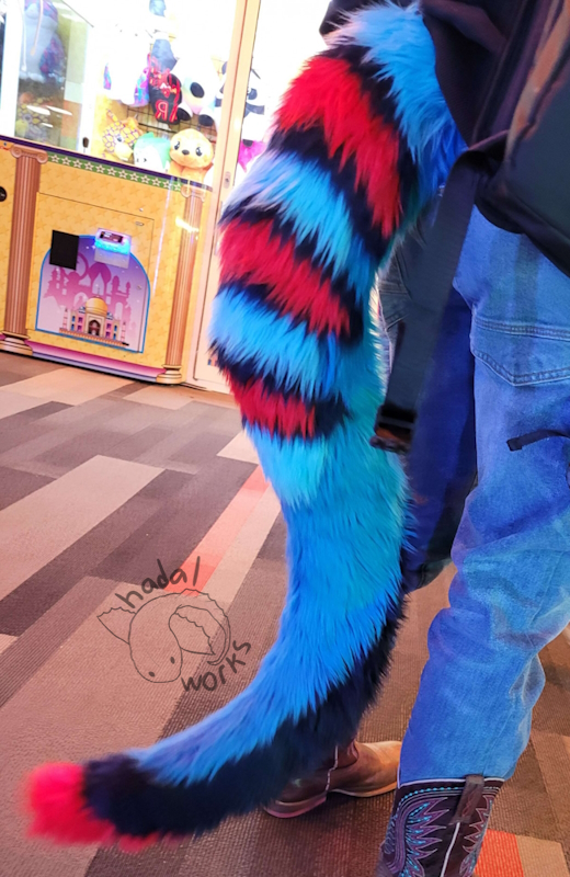 Photograph of a fursuit tail with a blue base and red stripes on the top and tail tip.