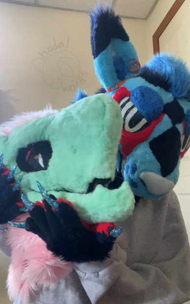 Blue kangaroo partial fursuiter holding up a clunkier lower quality green dragon fursuit head.