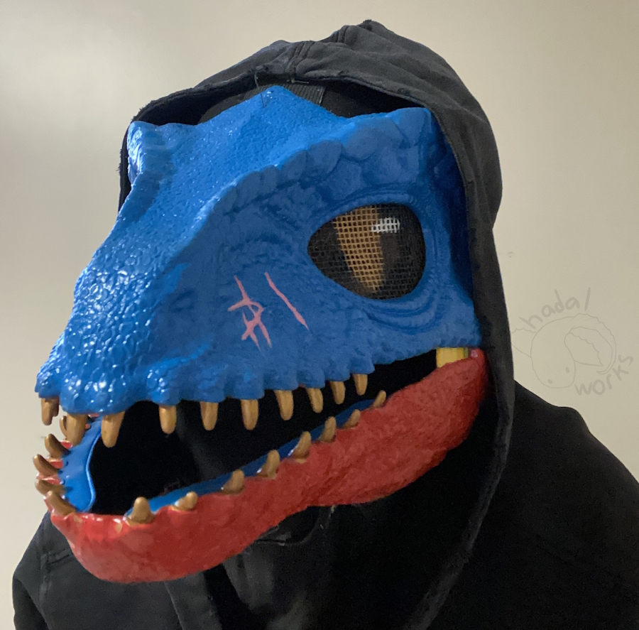 The mask at a nearly 3/4ths angle with the mouth open, showing its shiny teeth and how its lower gums are blue. At this angle, you can see a pink scar on the side of its face.