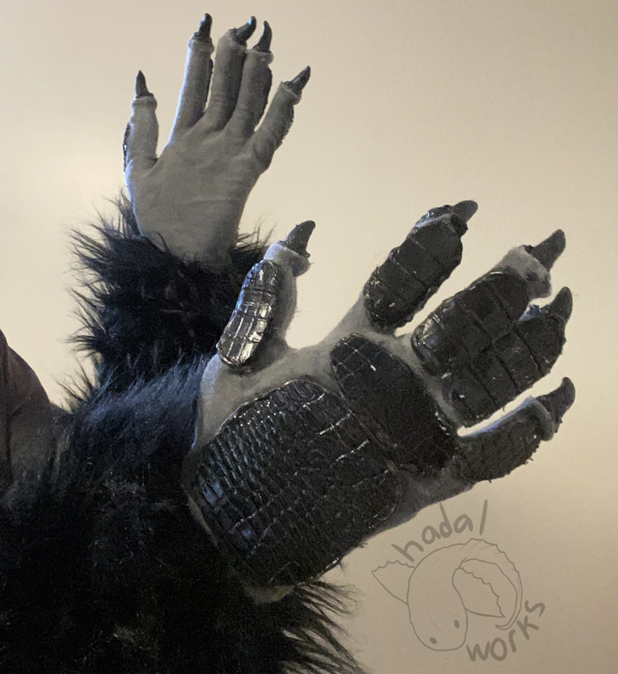 Two black gloves made to look like an anthropomorphic crow's hands. The gloves are gray with sharp black nails coming off them. The back of the hands has painted black pleather scales. The arms are pitch black long fur.