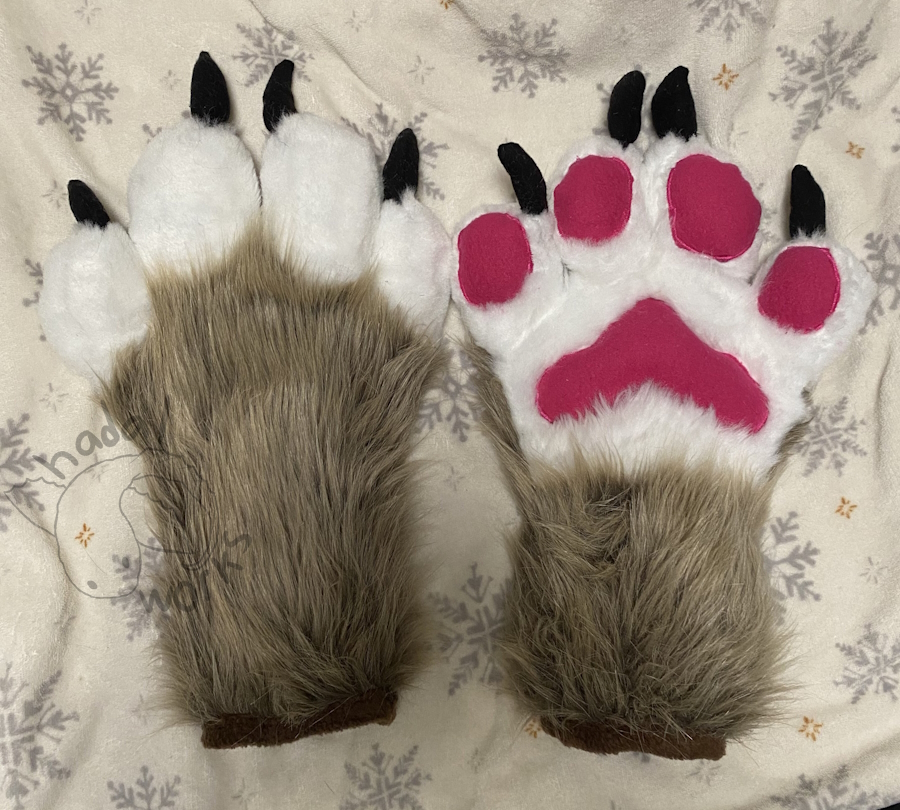 A pair of scrappy looking fursuit paws. They're brown with white palms, deep pink paw pads, and black claws.